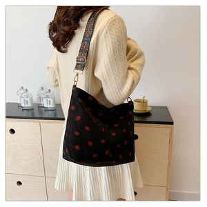 Close-up of strawberry embroidery on black corduroy bucket bag with patterned strap