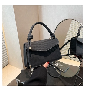 Detail of black woven texture handbag with knotted handle and elegant metal accents