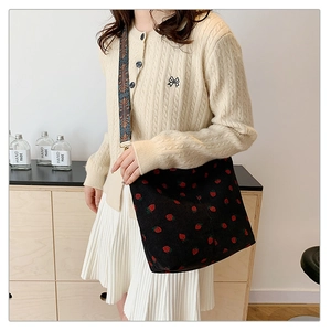 Black corduroy bucket bag with strawberry embroidery and a wide ethnic strap on model