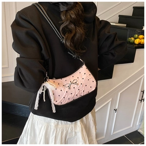 Chic pink leather shoulder bag with heart patterns and metallic bow detail worn by model
