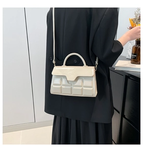 Detail of cream white handbag featuring a quilted chocolate grid pattern and top handle