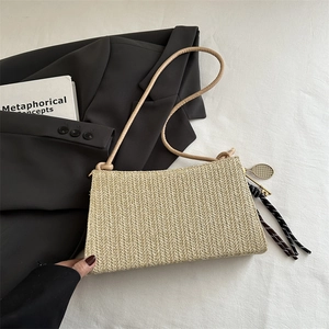 Bolso de hombro de paja trenzada con borla negra y colgante dorado de diseño