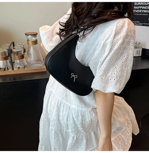 Detail of black hobo bag with silver bow accent shown in a trendy cafe setting