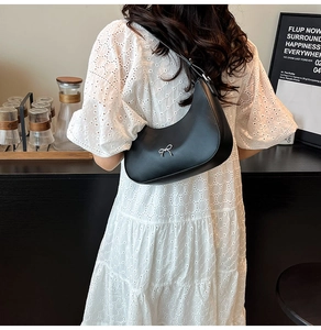 Detail of black crescent shoulder bag with silver metallic bow and smooth texture