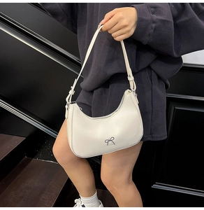Close-up of white hobo bag with a delicate black bow metal accent and adjustable strap