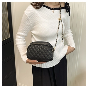 Close-up of black quilted shoulder bag with gold chain strap and dual zipper detail