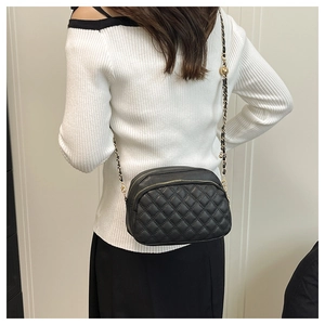 Detail of black quilted leather shoulder bag with gold chain strap on a model