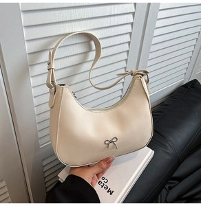 Close-up of a cream crescent shoulder bag with a silver metallic bow and smooth PU leather