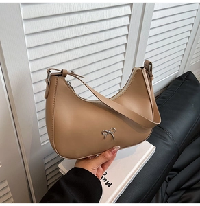 Detail of camel crescent bag featuring a silver bow accent and premium leather texture