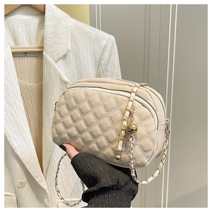 Détail du sac beige matelassé avec bandoulière en chaîne dorée et breloque boule en métal