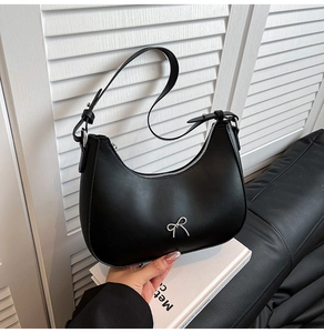 Detail of silver bow accent on black leather hobo bag with adjustable shoulder strap