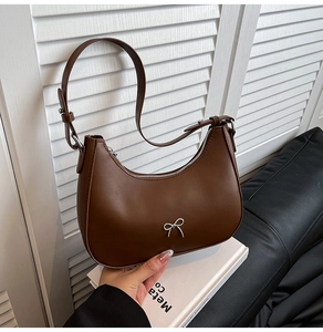 Detail of a brown crescent shoulder bag featuring a silver bow accent and leather texture