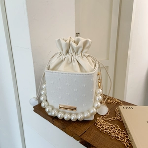 Detail view of white bucket bag featuring large pearl handle and golden chain strap