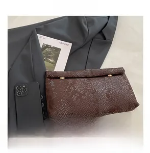 Macro detail of dark brown snakeskin embossed clutch featuring gold rivet accents