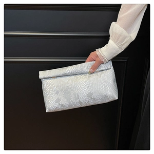 Detail view of silver snake-pattern clutch with magnetic snap buttons and textured finish