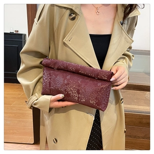 Close-up of deep burgundy envelope clutch with snake pattern texture held by a model