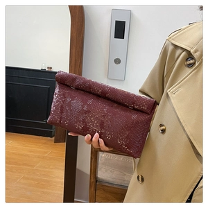 Detailed macro view of burgundy faux snake pattern texture on elegant folding clutch bag