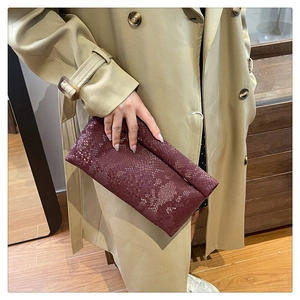 Close-up of a burgundy envelope clutch bag with snakeskin texture held by a woman