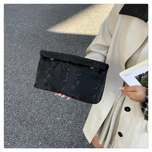 Detail of elegant black snakeskin textured envelope clutch with gold metal buckle