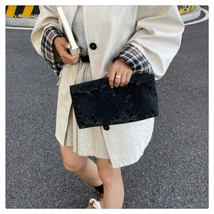 Close-up of black snake pattern embossed box bag held by model wearing a trench coat