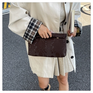 Detail of dark brown snakeskin texture envelope clutch bag held by woman in beige trench coat