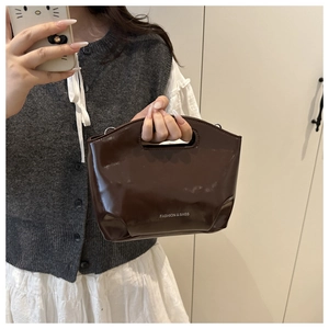 Mirror selfie showing a dark brown glossy trapezoid tote bag with cutout handle and text