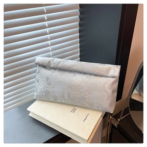 Macro shot of silver snakeskin texture clutch bag resting against a minimalist book