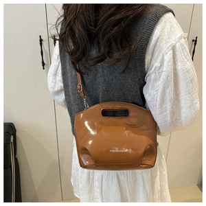 Detail view of brown patent leather handbag with adjustable strap and top handle
