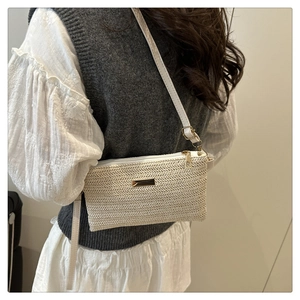 Detail of white woven straw crossbody bag with gold metal plate and textured wave pattern