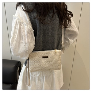 Detail view of a white woven crossbody bag showing metal zipper and adjustable strap