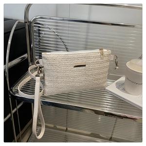 Detail view of woven cream straw crossbody bag with gold buckle on an acrylic shelf
