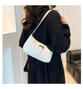 Close-up of a white leather trapezoid shoulder bag with gold metal clasp on a model