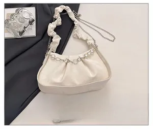 Detail view of cream pleated cloud bag with pearl chain next to a smartphone for scale