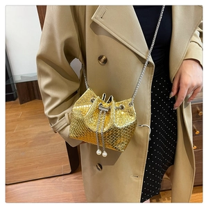 Detailed shot of golden woven bucket bag with pearl drawstring and silver chain strap