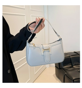 Details der hellblauen Leder-Sichel-Tasche mit goldener H-Schnalle in der Hand gehalten