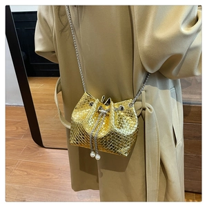 Detail of gold woven bucket bag featuring pearl drawstring charms and silver chain strap