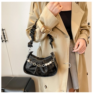 Detail of black pleated cloud bag featuring decorative pearl and floral metal chain