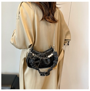 Detail of black pleated cloud bag featuring pearl and floral chain on a beige coat