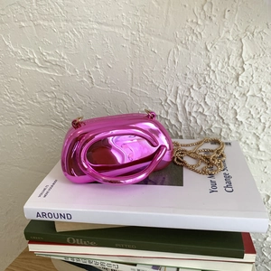 Mini rose pink metallic clutch with ring handle and gold chain strap on magazines