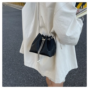 Detail of woven black bucket bag featuring silver chain strap and white pearl drawstring charms