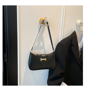 Close-up of matte black leather underarm bag with gold H-shaped buckle on a minimalist wall