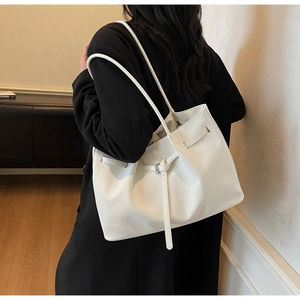 Detail of off-white tote bag with woven texture and buckle decoration on model