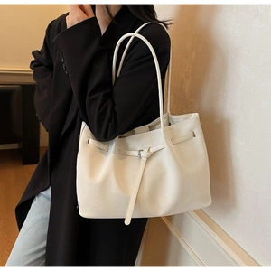 White tote bag with woven texture and metal buckle detail worn over a black suit
