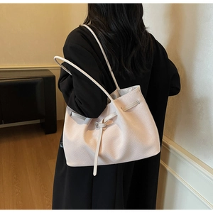Detail view of a beige woven leather tote bag with slender straps worn by a model