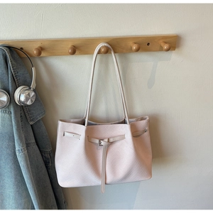 Pink woven tote bag with buckle detail hanging on a hook next to a denim jacket