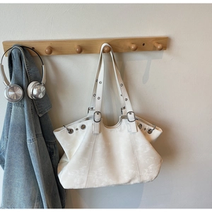 Chic white tote bag with silver eyelets and adjustable strap hanging in a cozy home setting