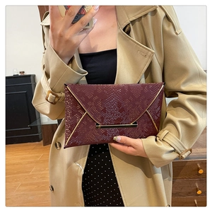Détail d'une pochette enveloppe bordeaux en peau de serpent avec garniture dorée