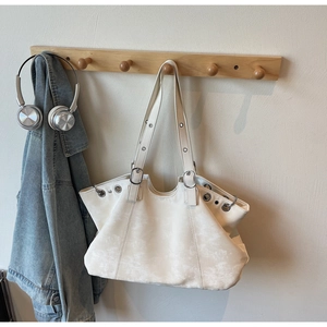 Detail of cream tote bag with silver eyelets hanging on a wooden hook with lifestyle props