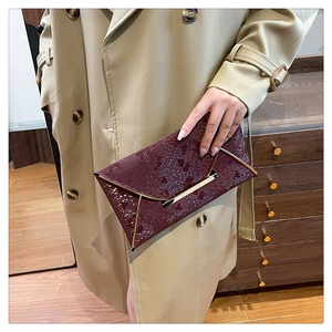 Close-up of wine red snake-embossed envelope clutch with elegant gold metal trim