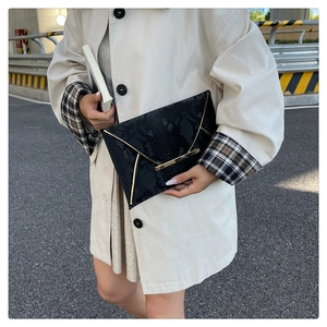 Close-up of black snake pattern envelope clutch bag with gold trim on beige coat